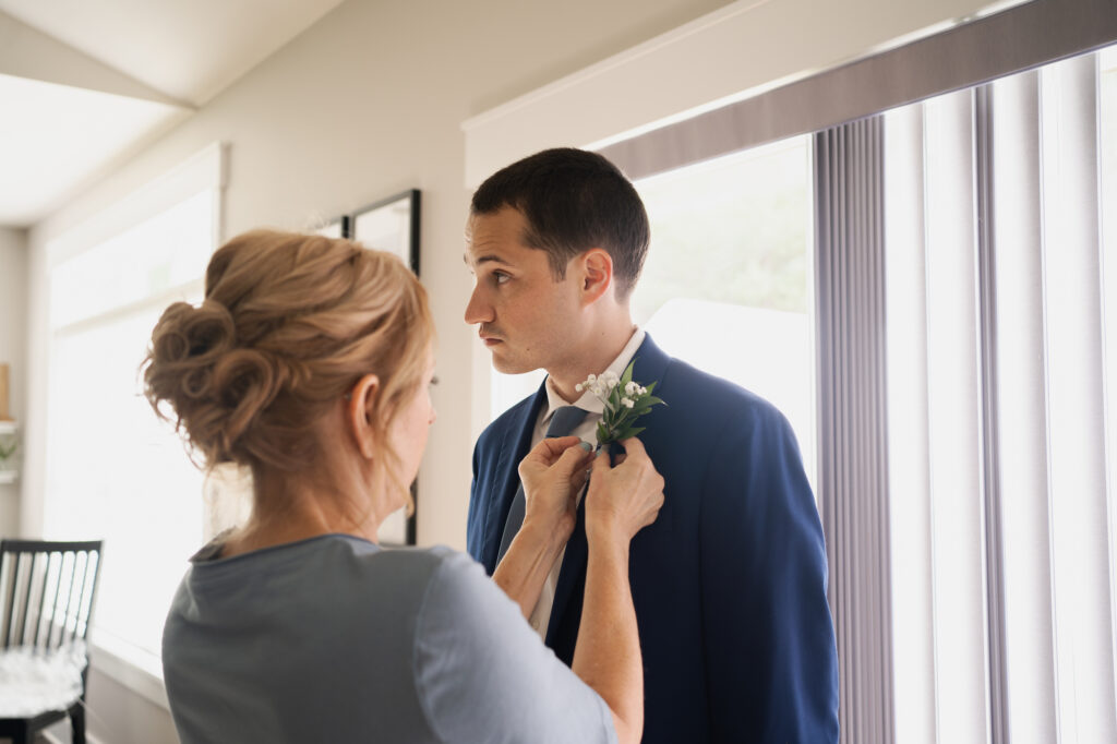 The groom's mom helping him pin his boutonniere. 