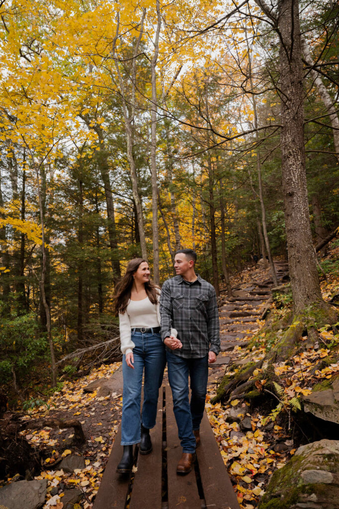 Aubrie and Dolan walking over a small bridge at Kaaterskill Falls during their engagement session in the Catskill Mountains.