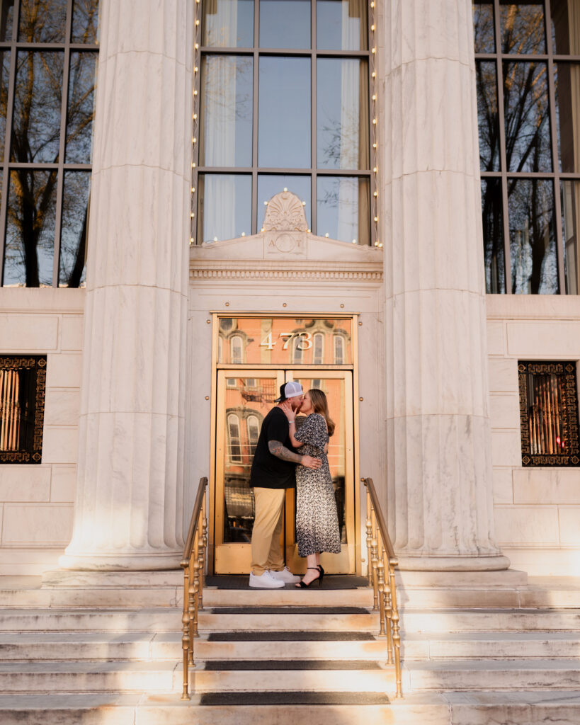 Sharing a kiss on the steps of Adirondack Trust in downtown Saratoga Springs during their engagement photos with Austin Ryan Photo.