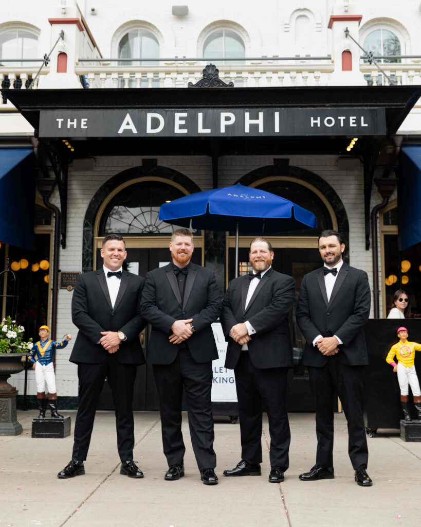 The groom and groomsmen pose for a photo in front of The Adelphi Hotel in Saratoga Springs.