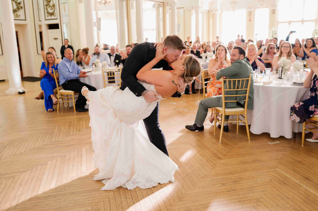 The bride and groom share a kiss on the dance floor, cheered on by their wedding guests at the Canfield Casino in Saratoga Springs, New York.