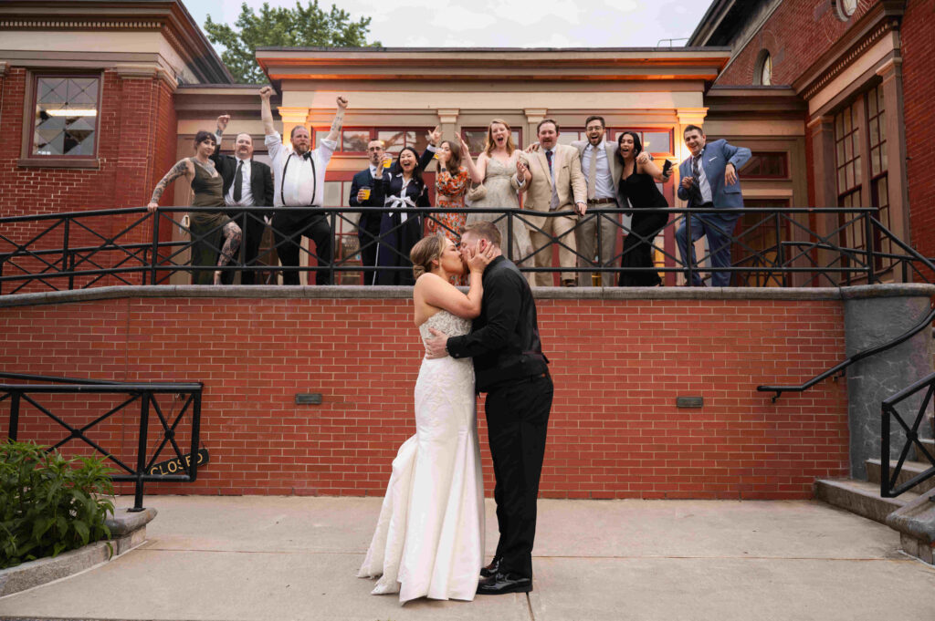 The bride and groom share a kiss cheered on by their guests outside of the Canfield Casino in Saratoga Springs, New York.