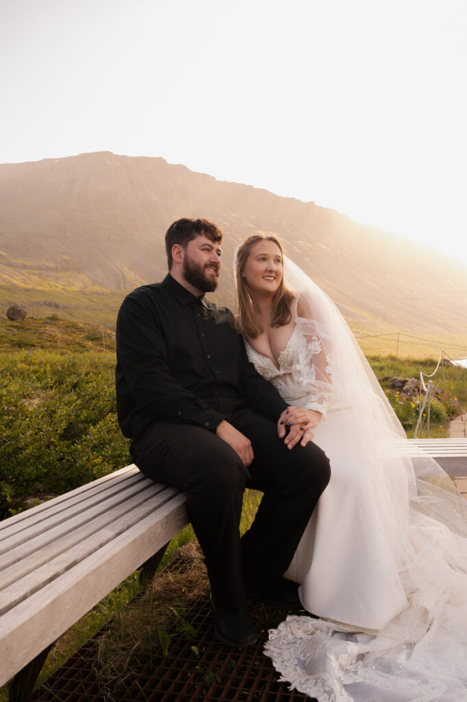 A portrait of the bride and groom sitting on a bench at Dynjandi Waterfall for their Iceland destination wedding photos.