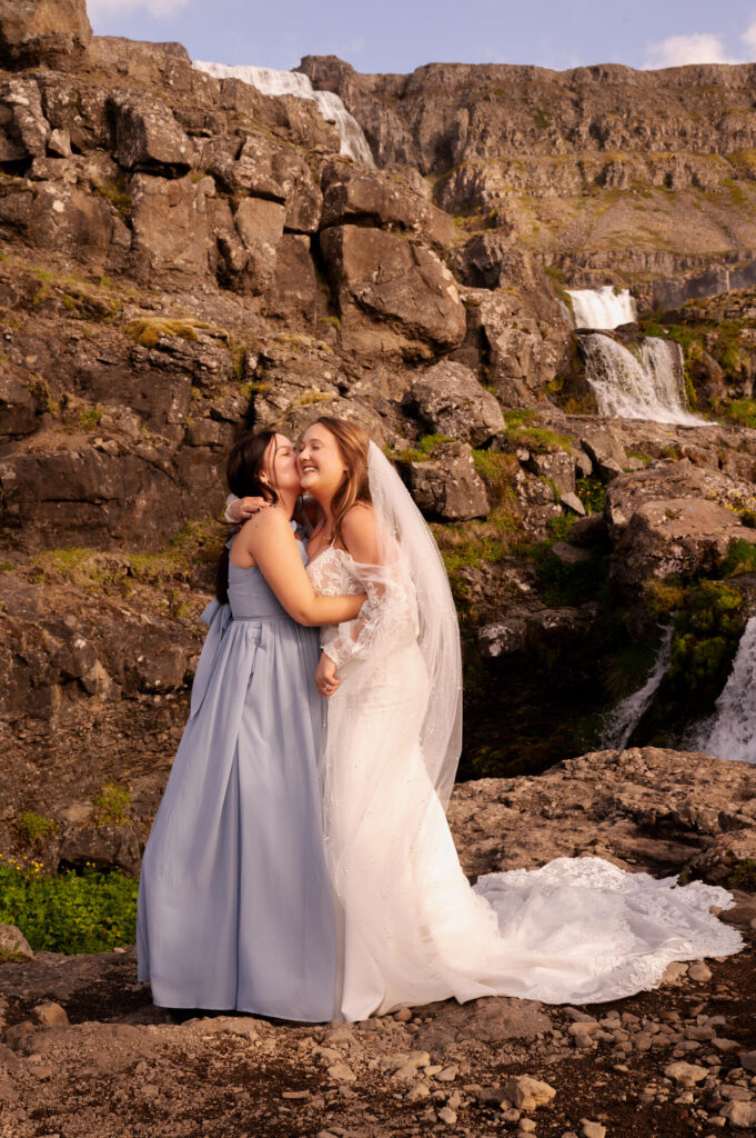 The bride sharing a hug with her bridesmaid at Dynjandi Waterfall for their Iceland destination wedding photos.