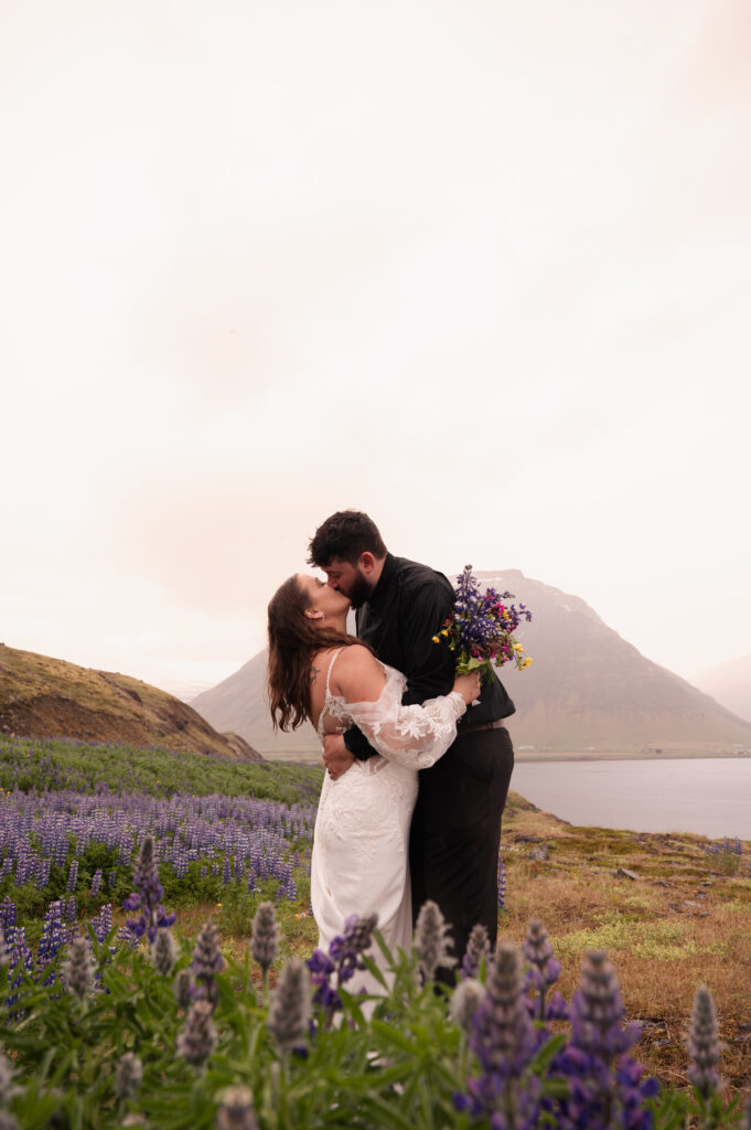 The bride and groom sharing a kiss in the lupines overlooking the Westfjords of Iceland during their Iceland destination wedding.