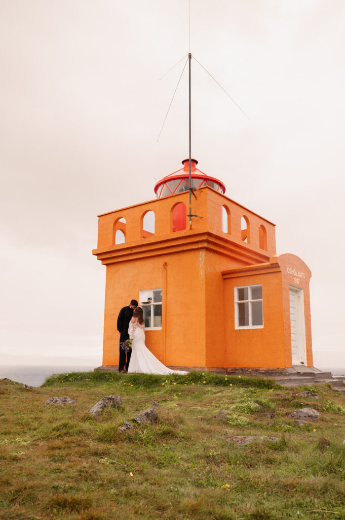 The bride and groom sharing a kiss underneath a lighthouse overlooking the Westfjords of Iceland during their Iceland destination wedding.
