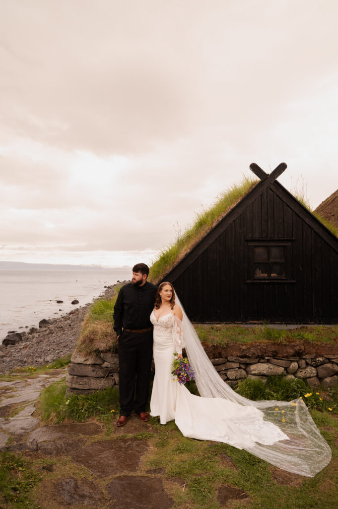 The bride and groom posing for a portrait at a fishing hut overlooking the Westfjords of Iceland during their Iceland destination wedding.